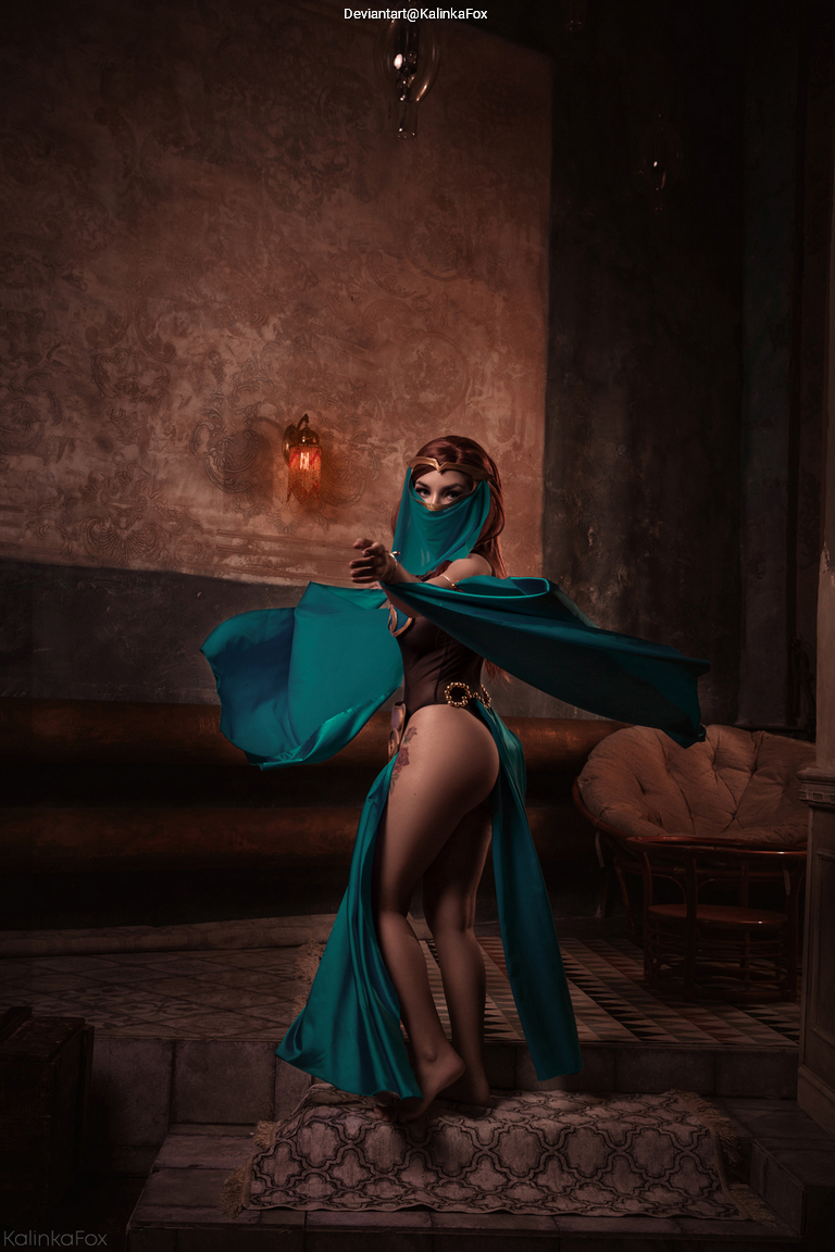 A woman wearing a teal scarf and revealing outfit poses gracefully in a dimly lit room with ornate decorations.