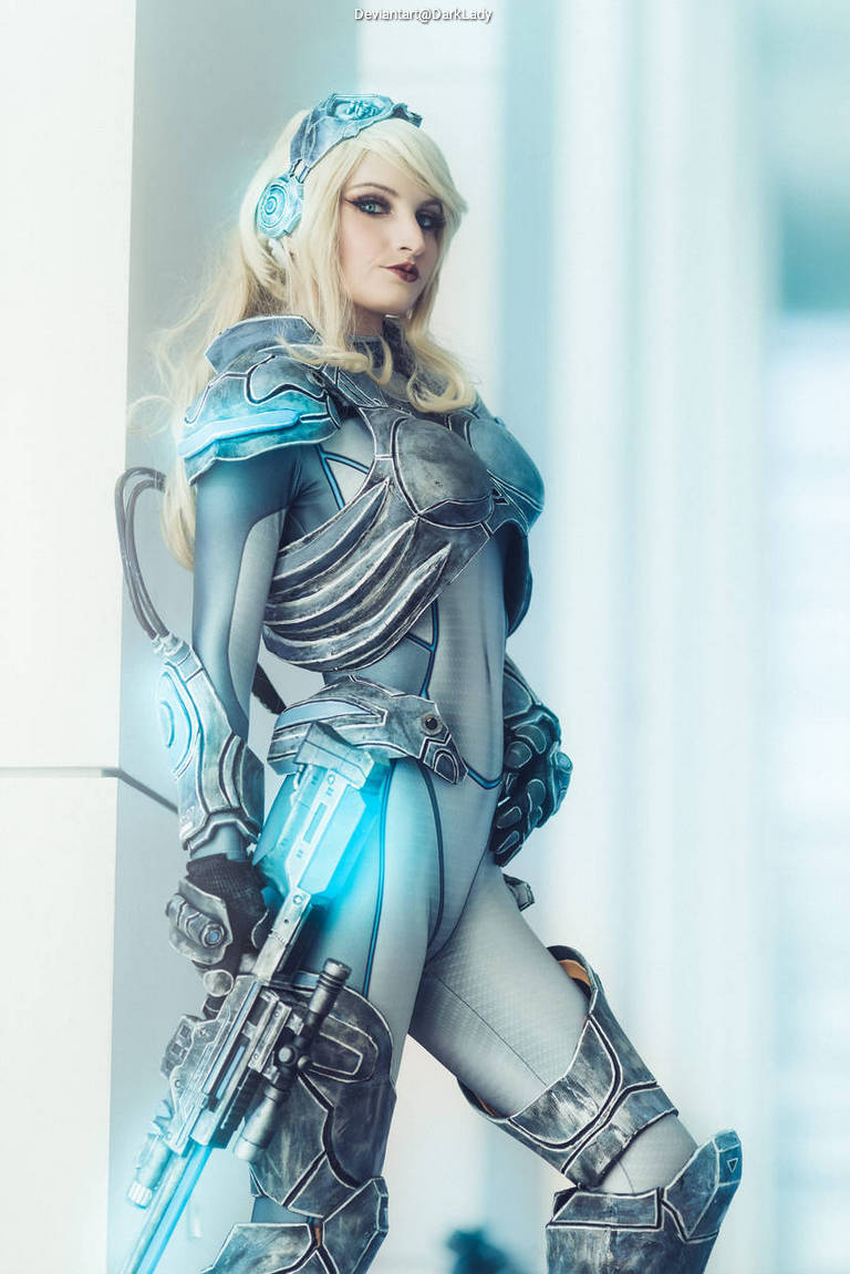 A female cosplayer in a futuristic armored suit, holding a sci-fi weapon, set against a bright, modern background.