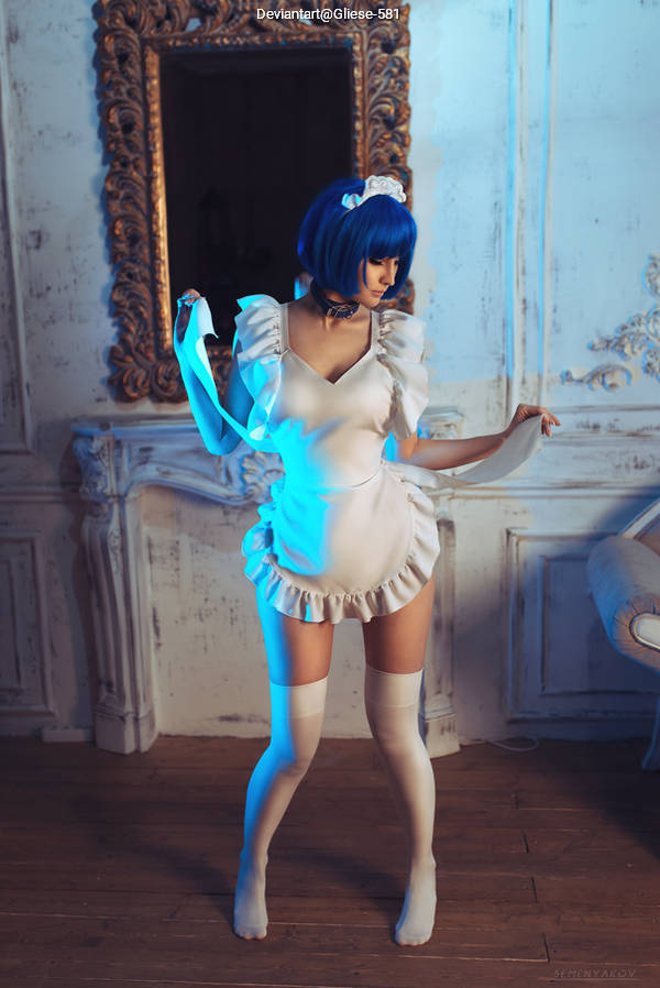 A person in a white dress with ruffles and thigh-high stockings, posing in a studio with blue lighting and an ornate mirror in the background.
