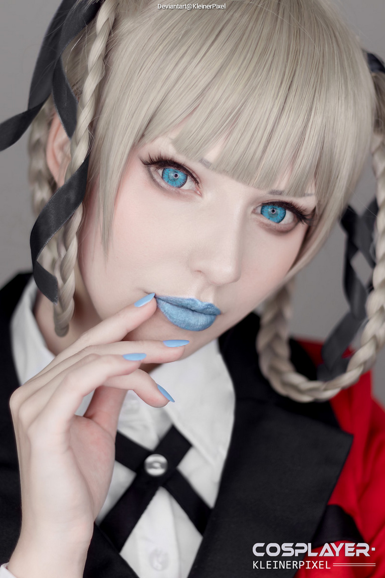 Close-up portrait of a person with pale blonde hair in braids, blue eyes, and blue lipstick, wearing a black and red outfit.