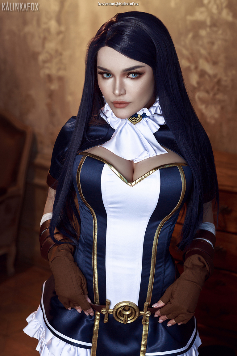 A woman dressed in a detailed blue and white costume with gold accents, featuring a high collar and gloves, posing confidently in a vintage setting.
