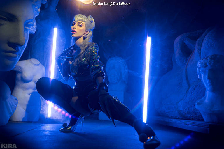 A female model in a striking pose, wearing a futuristic outfit with high heels, surrounded by classical statues and illuminated by blue lighting and neon accents.