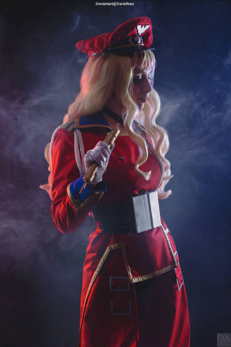 A person dressed in a red military-style costume with a matching hat, holding a baton, surrounded by smoke.