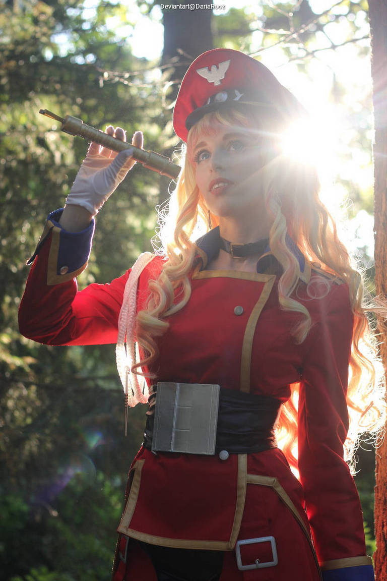 A woman wearing a red military-style costume with a hat, holding a flute in a forest setting, illuminated by sunlight.