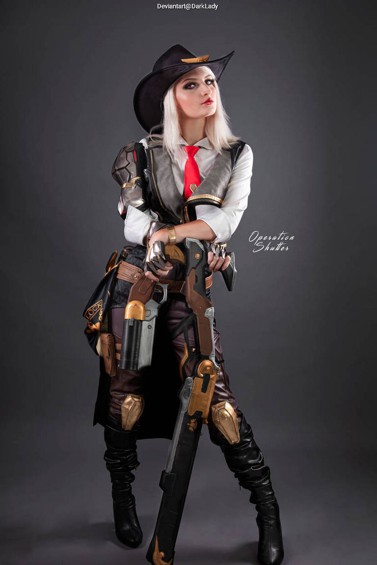 A person in a futuristic cowboy costume, featuring a hat, a white shirt, and dark leather pants, posing with a weapon against a dark background.