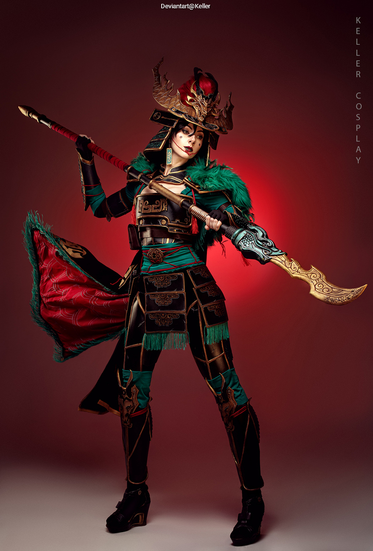 A person dressed in an elaborate cosplay outfit inspired by historical armor, featuring vibrant green and black colors, holding a decorative weapon, posed against a dramatic red background.