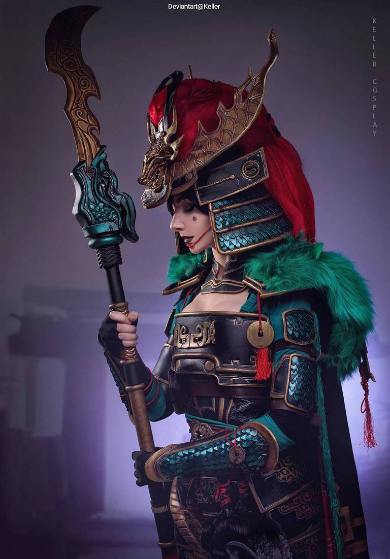 A female cosplayer dressed in elaborate armor inspired by ancient warriors, featuring a dramatic red wig, a detailed helmet with a dragon motif, and a staff in her hand. The background has a mystical, foggy ambiance.