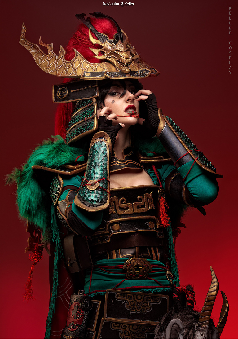 A person in elaborate cosplay featuring a detailed armor set, including a dragon-adorned helmet and rich green and red accents, posing against a red background.