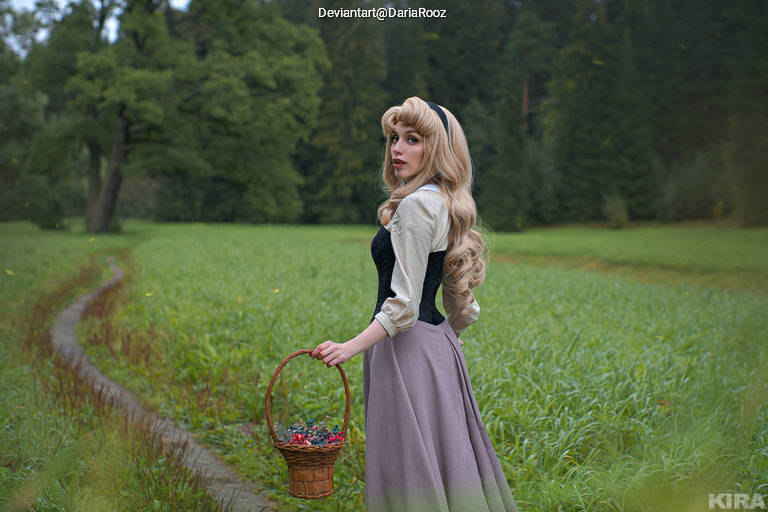 A woman with long blonde hair wearing a black and cream outfit stands in a lush green field, holding a basket filled with berries.