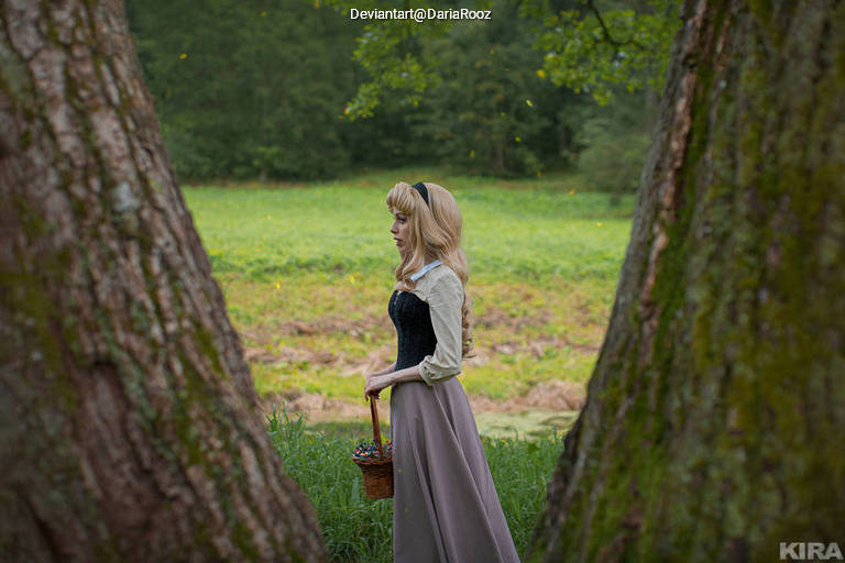 A woman dressed in a historical outfit stands between two large trees, holding a basket, with a lush green field in the background.