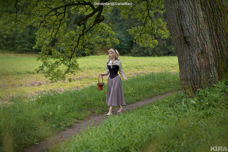 A woman in a vintage dress walking on a path in a lush green field, carrying a small basket.