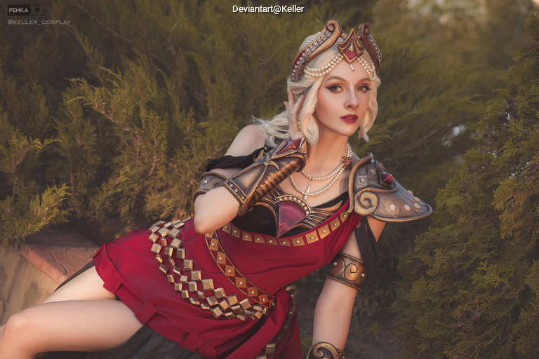 A woman in a fantasy-inspired costume with armor and a red dress, posing outdoors surrounded by greenery.