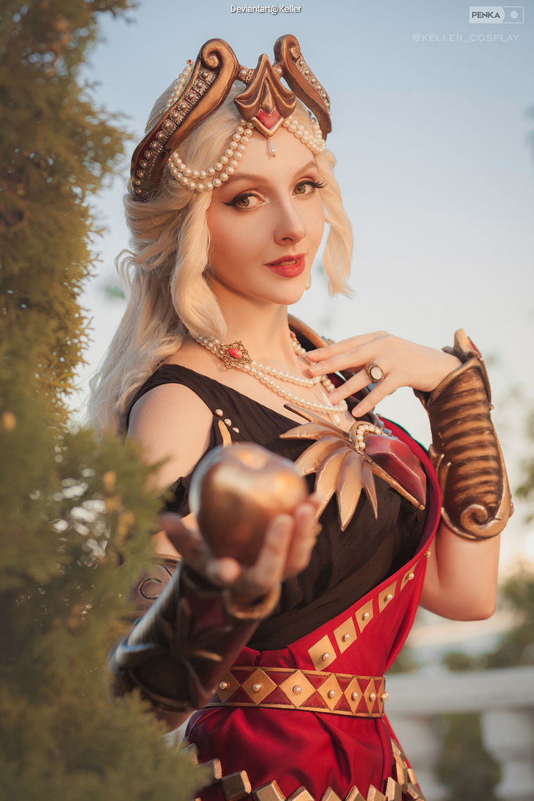 A person dressed as a character in a regal costume, wearing a crown and holding an apple, poses confidently outdoors.