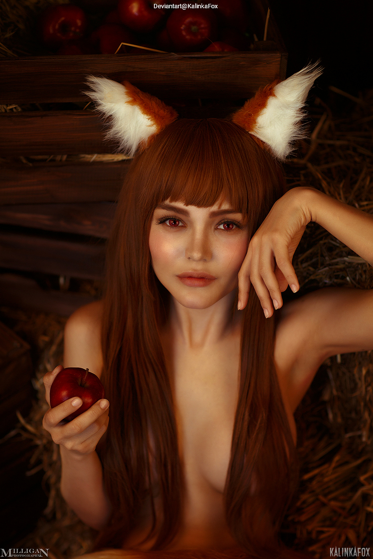A person with long brown hair and fox ears, holding an apple, posed in a rustic setting with hay and wooden crates in the background.
