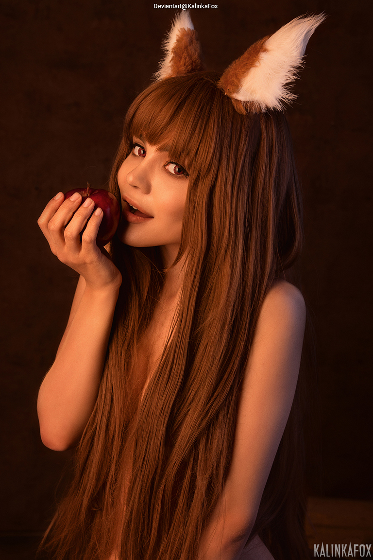 A person with long, brown hair and fox ears is holding an apple close to their face, appearing playful and slightly mischievous.