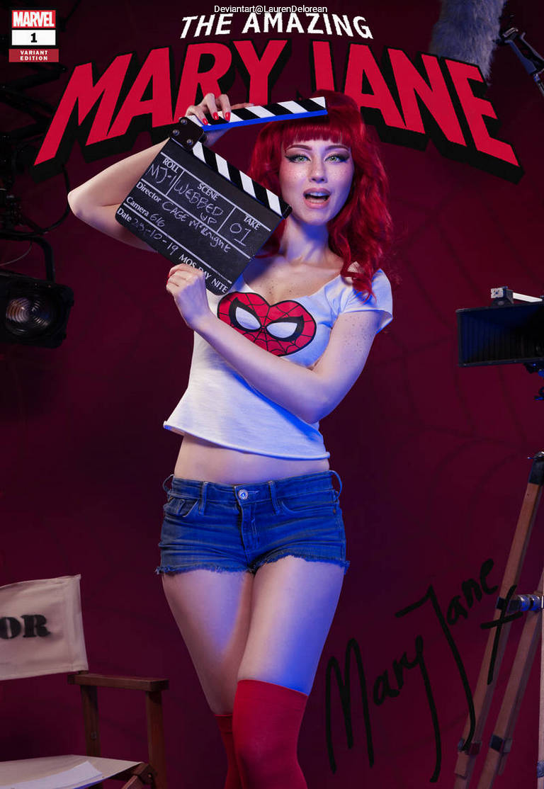A woman with red hair wearing a Spider-Man themed shirt and shorts holds a film clapperboard, standing in front of a movie set backdrop with colorful lighting.