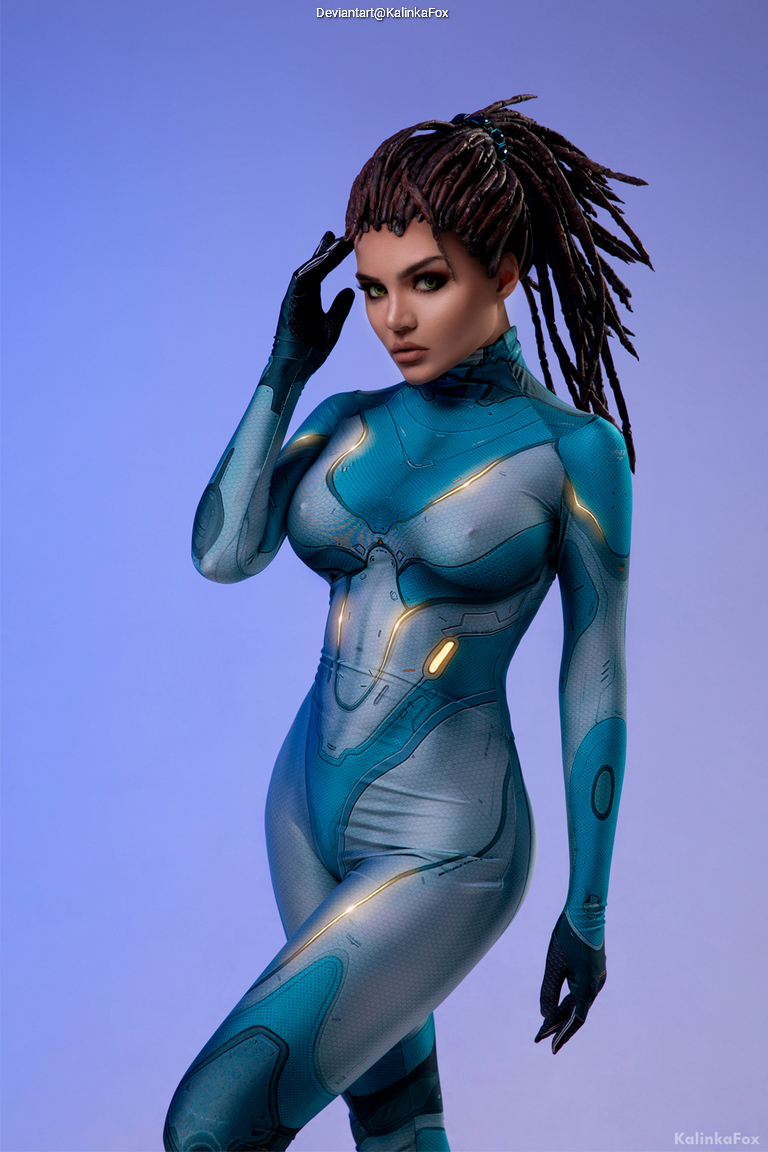 A model poses in a form-fitting, futuristic blue bodysuit with intricate designs, showcasing a sci-fi-inspired look.