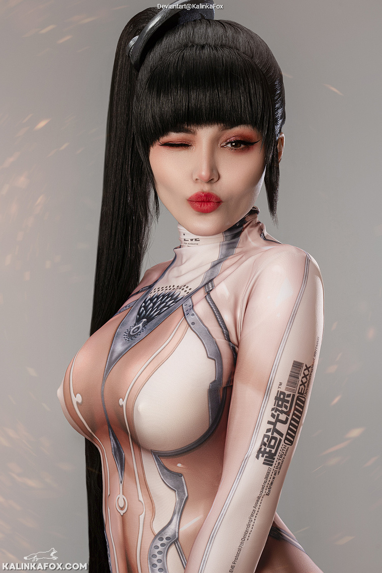 A woman with long black hair styled in a ponytail, wearing a form-fitting, futuristic outfit that features intricate designs and patterns. She is winking playfully at the camera.