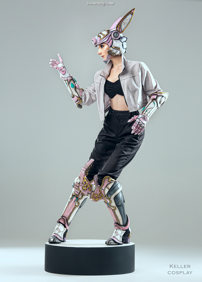 A person in a futuristic cosplay outfit featuring intricate armor details and a unique helmet, striking a pose on a pedestal.