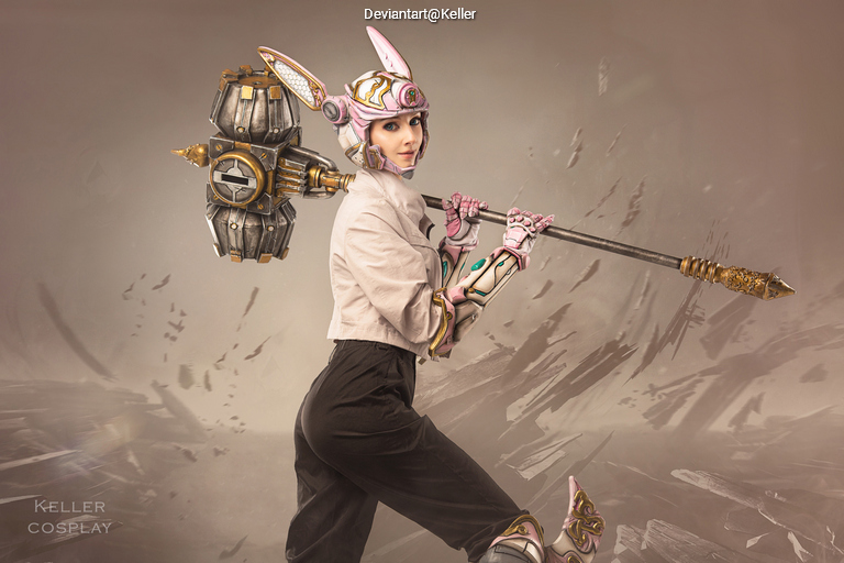 A female cosplayer dressed in a fantasy-themed costume featuring pink and metallic elements, wielding a large, ornate weapon. The background is blurred with abstract patterns, emphasizing the character's dynamic pose.