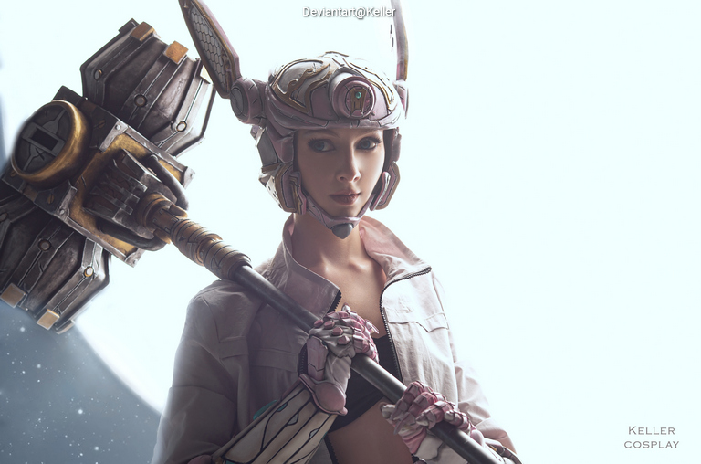 A person in a detailed cosplay outfit, featuring a decorative helmet and holding a large hammer, stands in front of a bright, soft background.