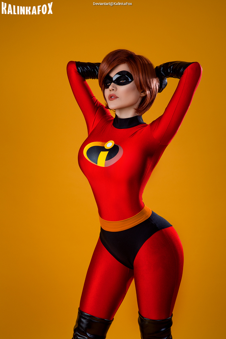 A woman posing confidently in a red superhero costume with a black eye mask on a yellow background.