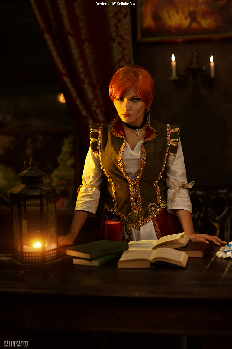 A person with orange hair in a historical costume stands at a wooden table with books, a lit lantern, and a candle. The background features dim lighting and decorative fabric.