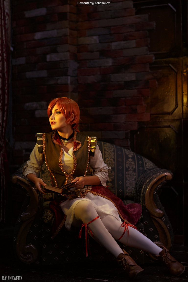 A person with short red hair dressed in a historical-themed costume is sitting on a vintage sofa while reading a book, surrounded by a rustic interior.