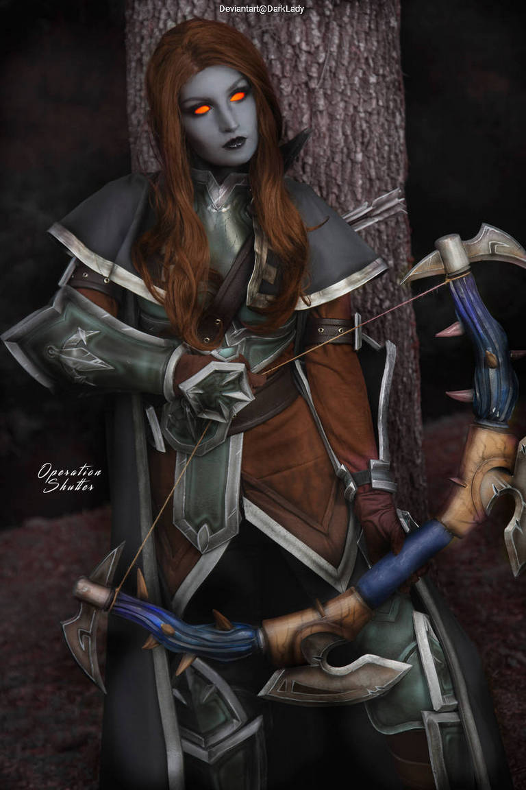A fantasy character with gray skin and glowing orange eyes stands leaning against a tree, holding a decorated bow. The character wears an elaborate outfit with metallic accents and long, wavy brown hair.