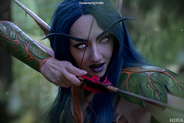 A fantasy character with blue hair and elaborate green armor is drawing a bow, focusing intently, in a lush, natural setting.