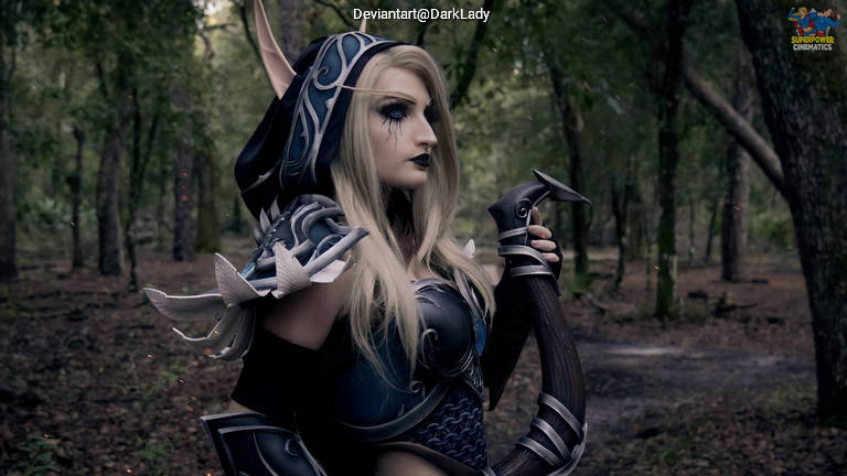 A woman with long blonde hair and pointed ears, wearing dark fantasy armor and a hood, holding a curved staff in a forest setting.