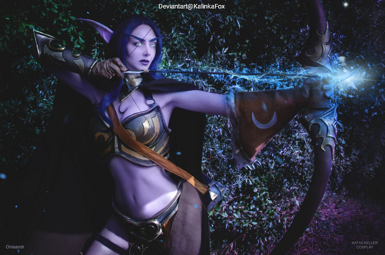 A female cosplayer dressed as an archer character, holding a bow and preparing to shoot an arrow, with glowing magical effects around her hand. The background features dark foliage and mystical lighting.