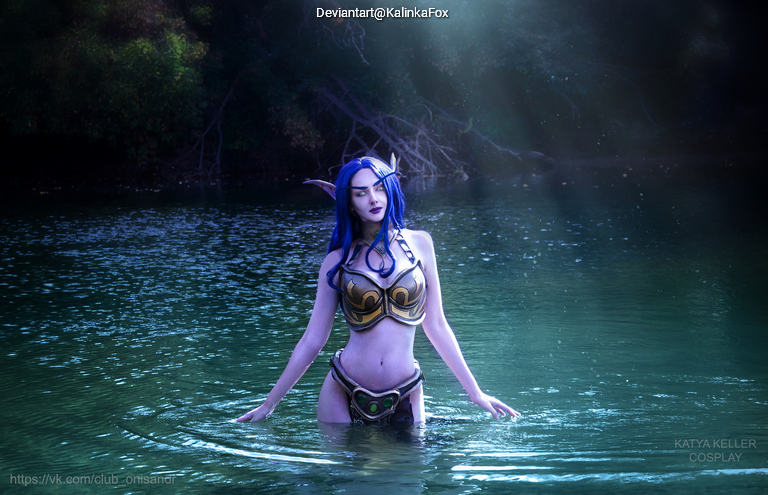 A character in a fantasy-themed costume standing in a body of water, with blue hair and elaborate armor. Natural lighting highlights the scene.
