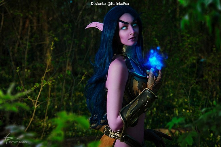 A fantasy character with long dark blue hair and pointed ears, wearing armor, holding a glowing blue orb in a natural outdoor setting.