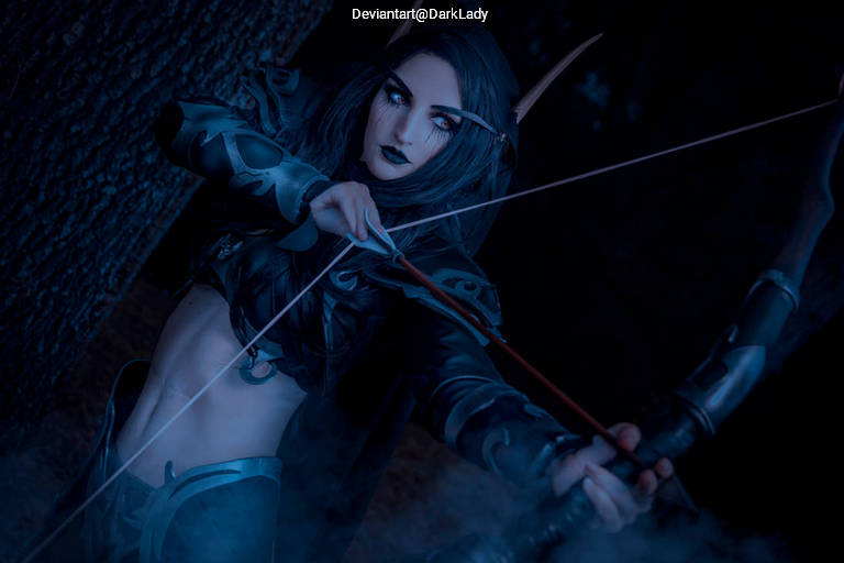 A female archer in a dark, fantasy-inspired costume, holding a bow and preparing to shoot an arrow, surrounded by a misty forest backdrop.