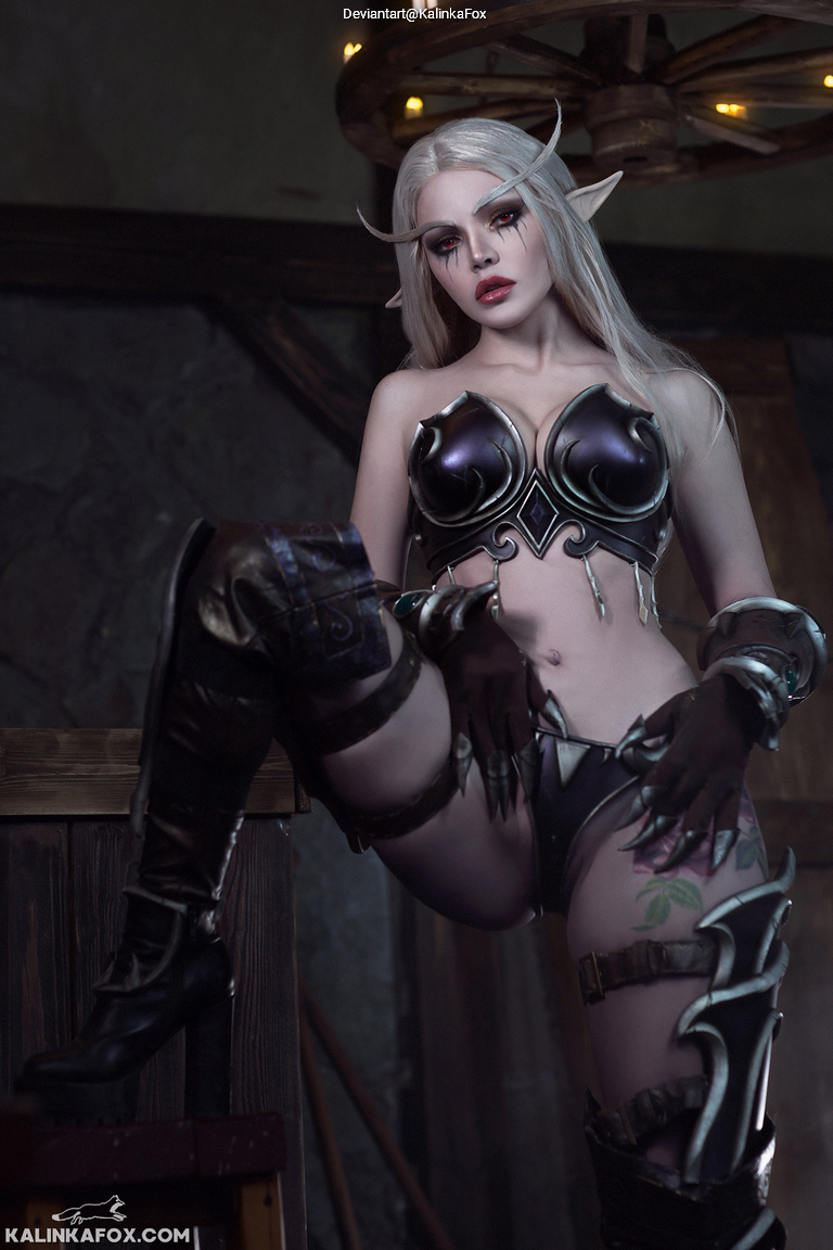A fantasy character with long silver hair and pointed ears, wearing intricate dark armor and thigh-high boots, poses in a rustic setting with wooden elements.