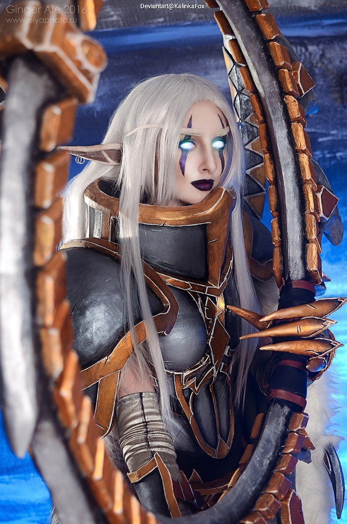 A cosplayer dressed as a fantasy character with long white hair, glowing eyes, and intricate armor holding a large ornate mirror.