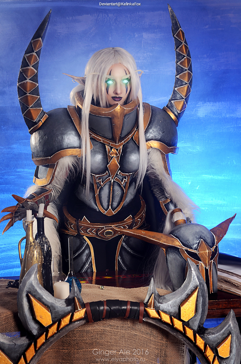 A person dressed in elaborate fantasy armor with sharp horns and glowing eyes, posing dramatically in front of a blue backdrop.