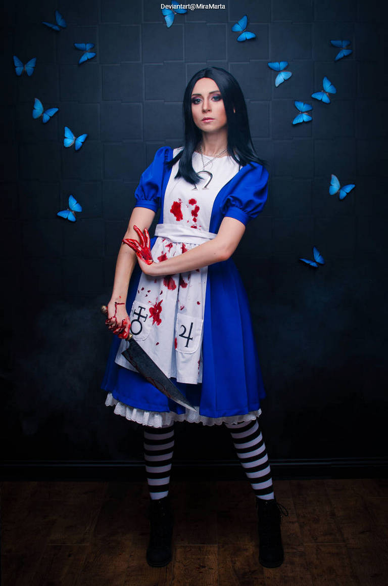A woman dressed as a dark-themed version of Alice from 'Alice in Wonderland,' wearing a blue dress with blood stains, holding a knife, and surrounded by blue butterflies against a dark background.
