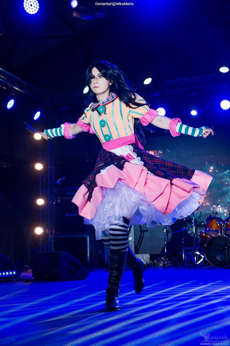 Person in a colorful dress performing on stage with dramatic lighting.