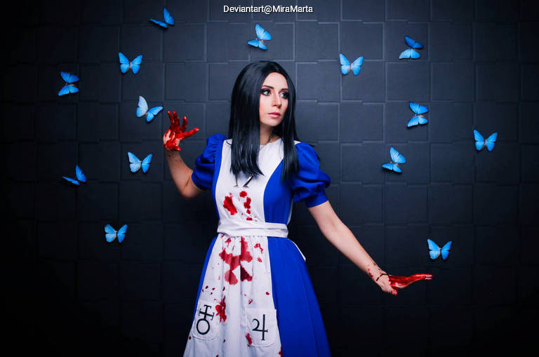 A person in a blue and white dress with blood stains poses against a dark wall decorated with blue butterflies.