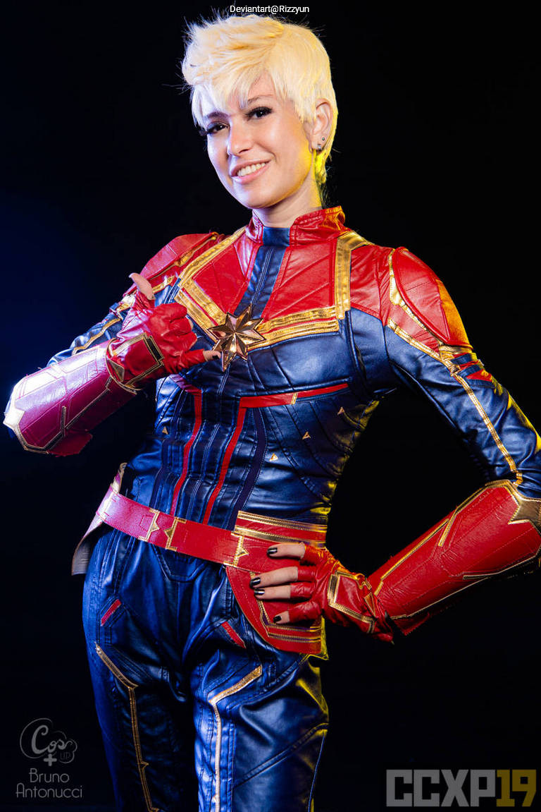 A person posing in a colorful superhero costume with red and blue elements, reminiscent of a comic book character. They are smiling and making a thumbs-up gesture.
