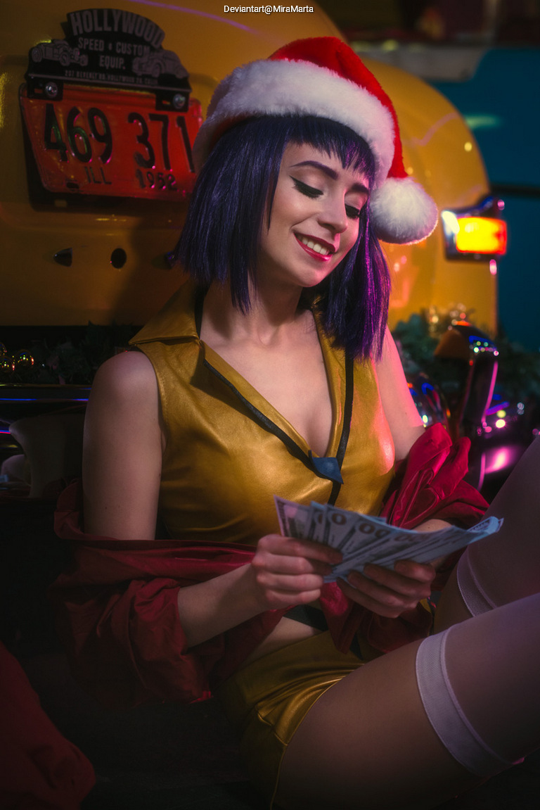 A woman with short purple hair wearing a Santa hat and a shiny yellow outfit is holding dollar bills while sitting next to a decorated taxi.