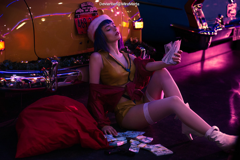 A woman in a festive outfit with a Santa hat sits on the floor next to a bright yellow vintage car, surrounded by scattered play money and a red sack.
