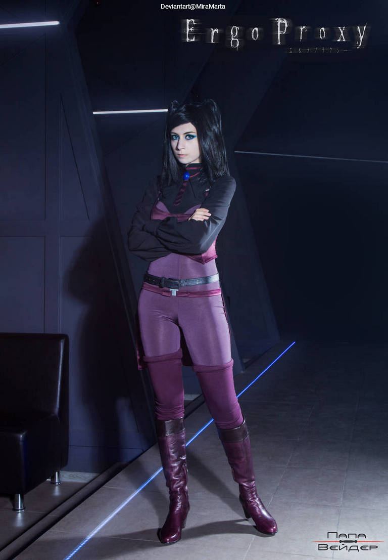A person dressed as a character from Ergo Proxy, standing confidently in a futuristic setting, with long black hair and vibrant blue eye makeup, wearing a sleek, purple outfit and high boots.