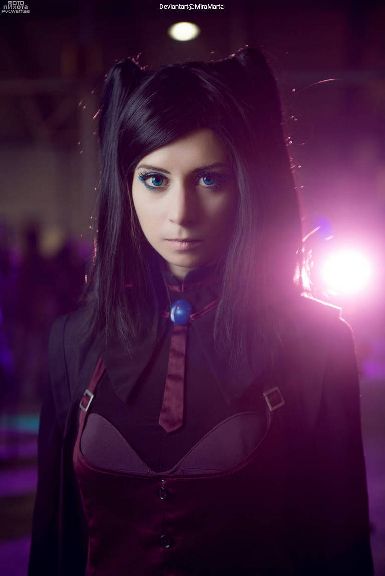A close-up portrait of a woman with long black hair styled in cat ears, wearing a dark outfit with a purple accent, and striking blue eyes, illuminated by soft purple and pink lighting.