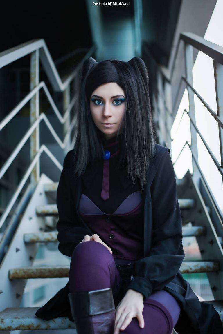 A person with long black hair styled with two pigtails, wearing a dark purple outfit, seated on metal steps in an industrial setting.