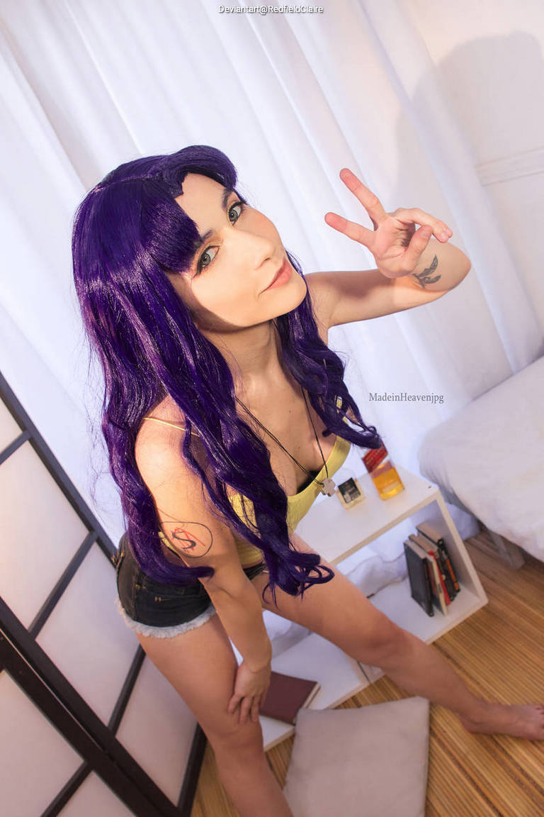 A person with long purple hair posing playfully while wearing a tank top and shorts, making a peace sign with their right hand.