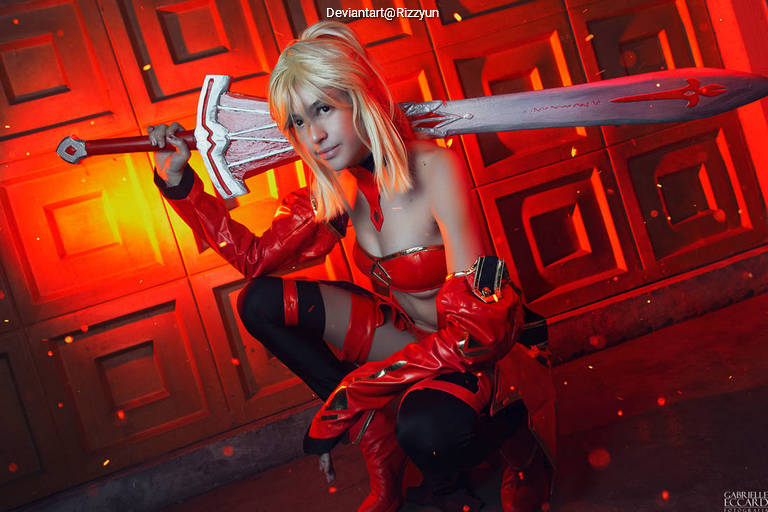 Cosplayer dressed in a red outfit, wielding a large sword, posed dramatically against a warm-toned background.