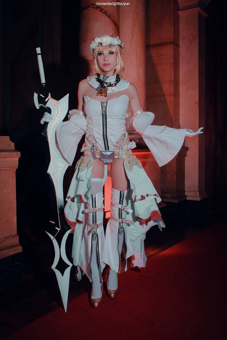 A person in a fantasy-themed costume, featuring a white dress with flared sleeves and thigh-high boots, holding a large ornate sword in an elegant indoor setting.